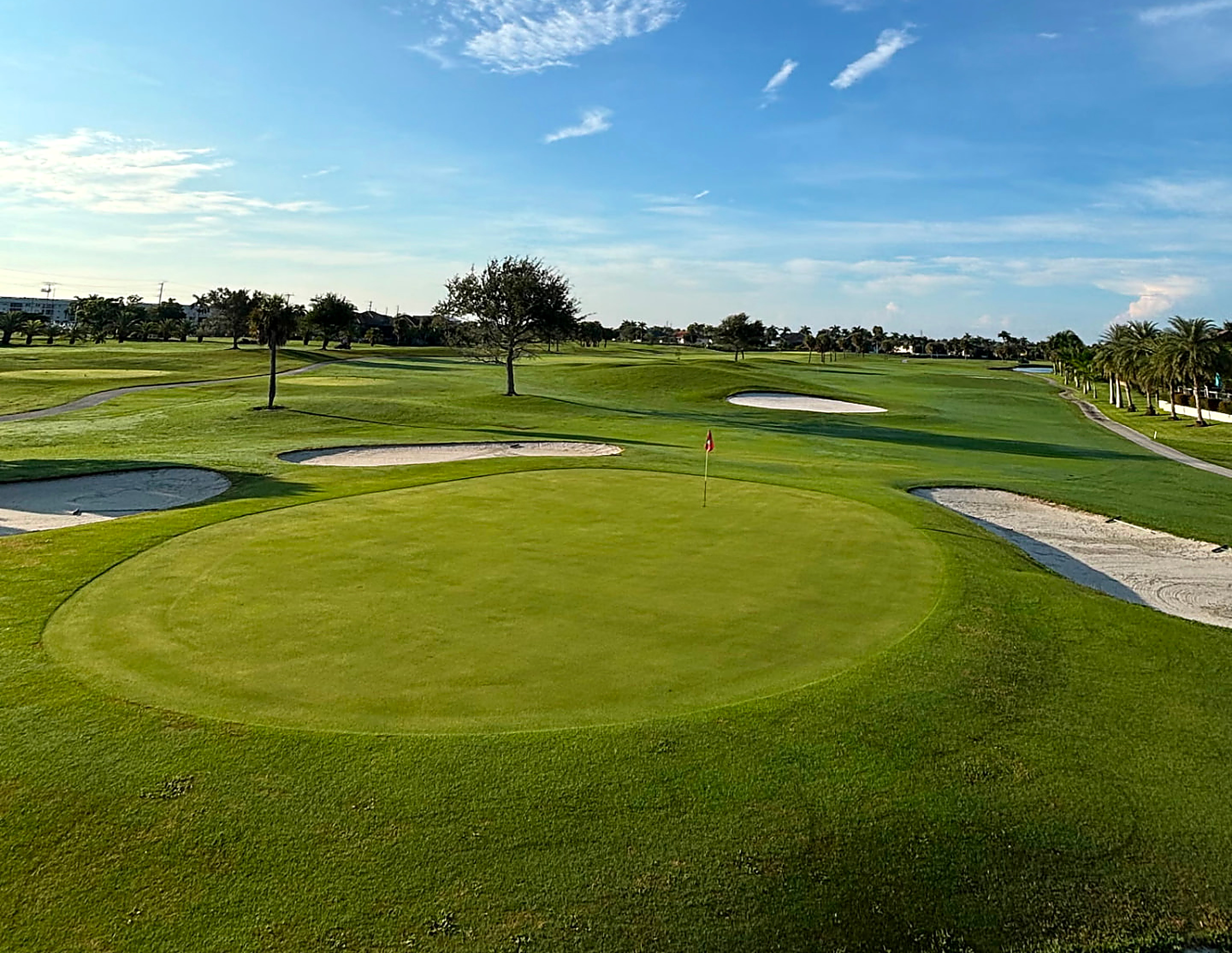 Manicured green with red flagstick, bunkers and palms at St. Andrews South Golf Club